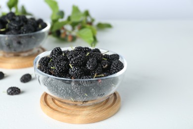 Delicious ripe black mulberries in glass bowl on white table, closeup