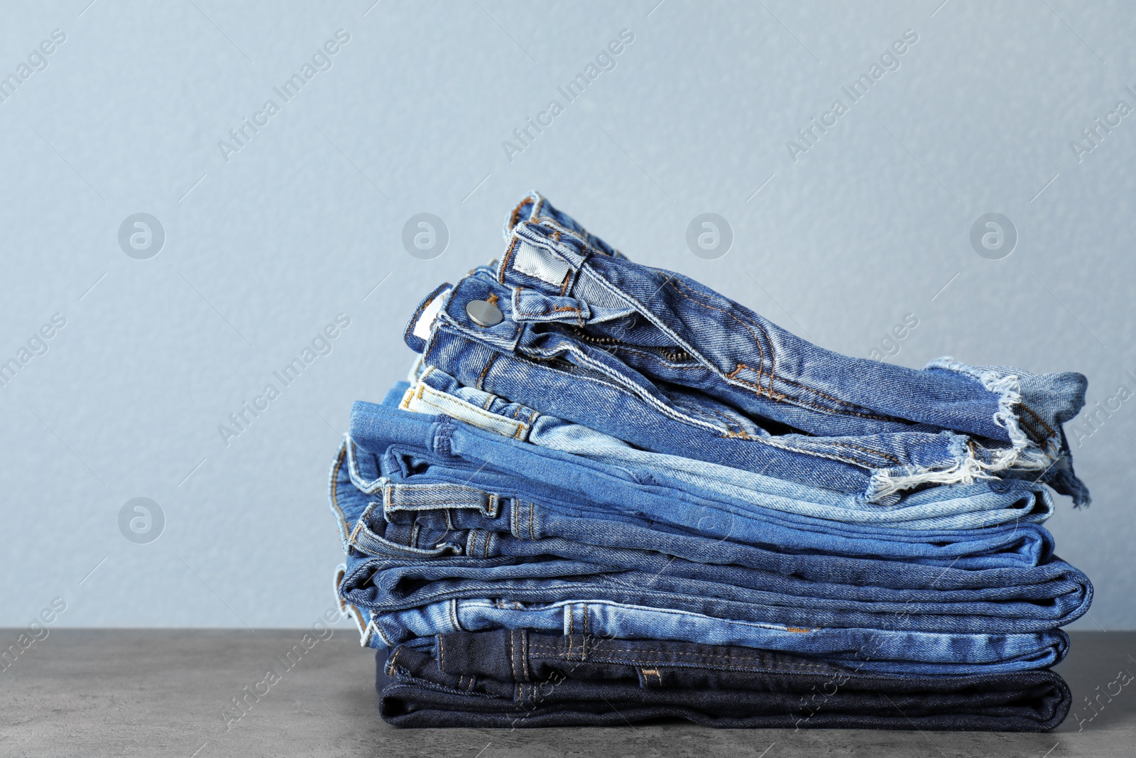 Photo of Stack of jeans on table against grey background