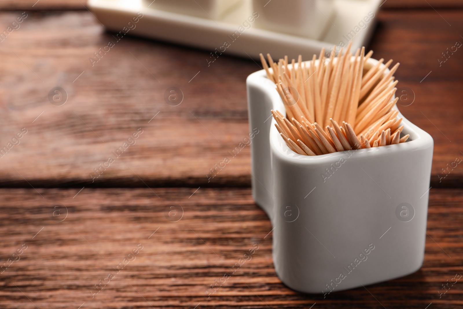 Photo of Holder with many toothpicks on wooden table, closeup. Space for text