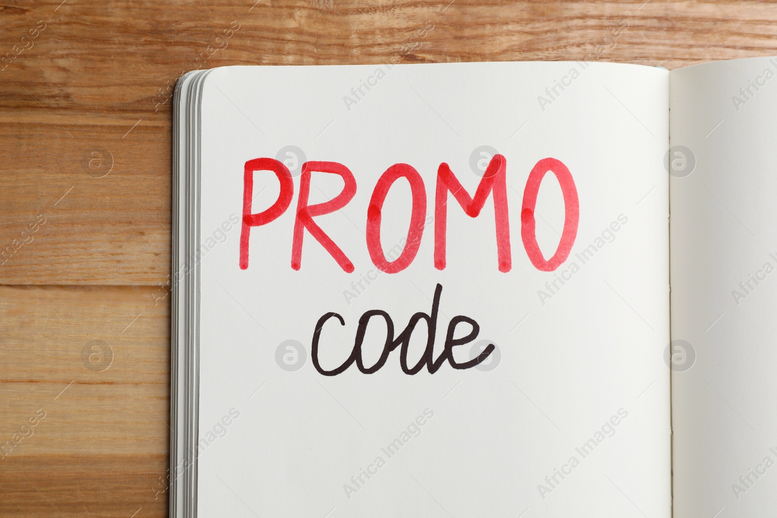 Photo of Notebook with words Promo Code on wooden table, top view