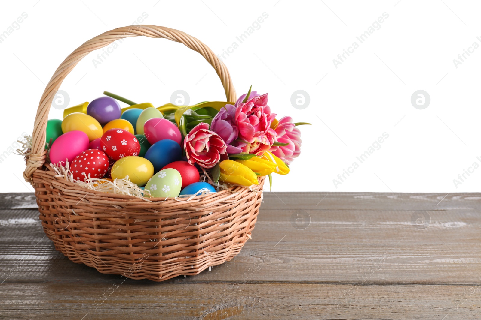 Photo of Colorful Easter eggs in wicker basket on wooden table against white background