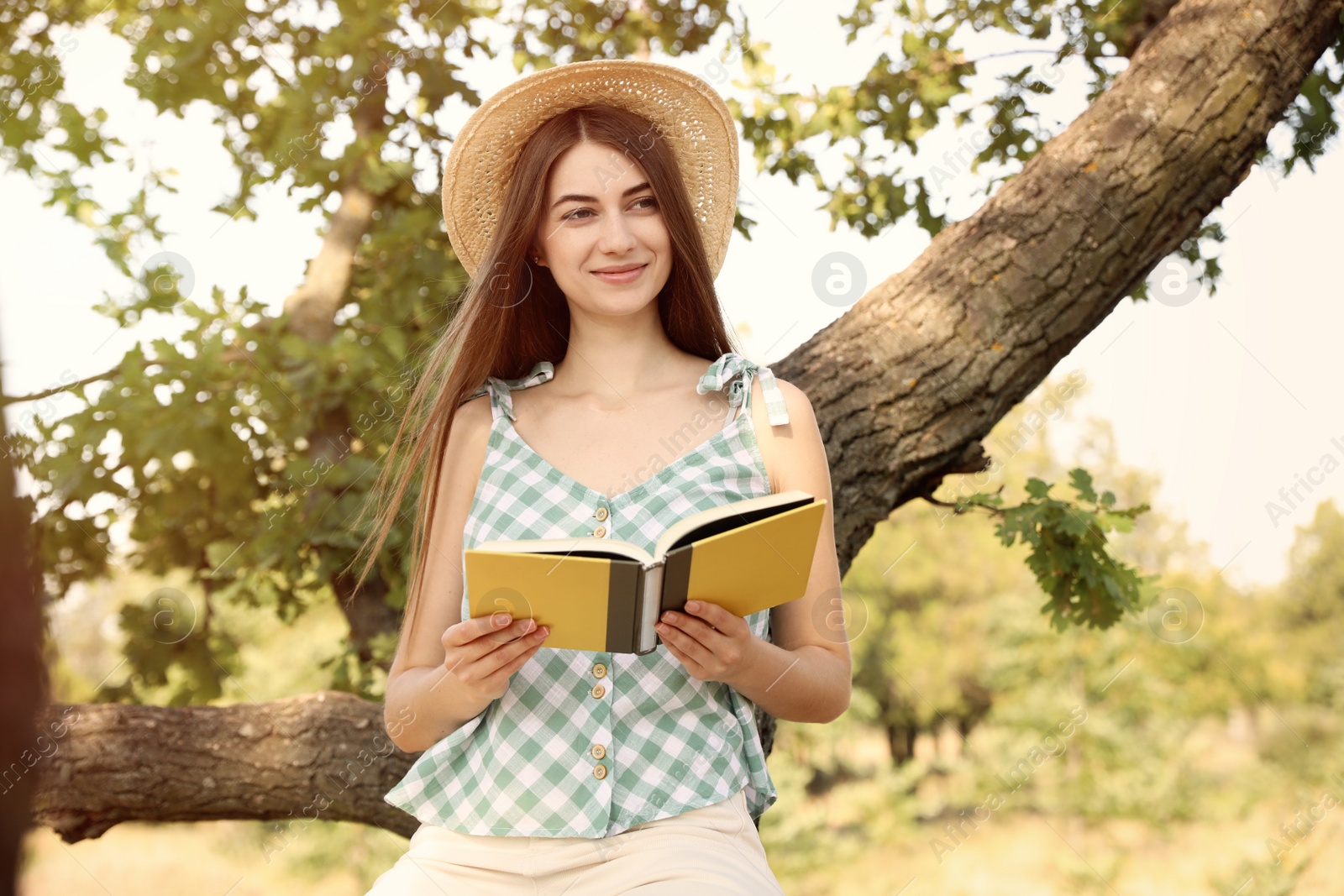 Photo of Young woman reading book near tree in park