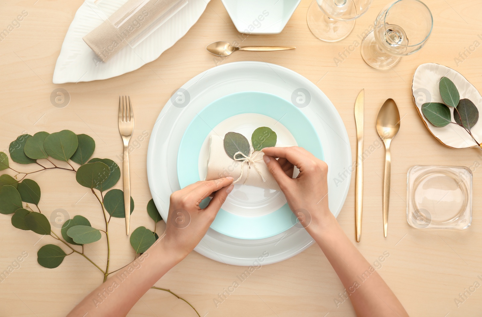 Photo of Woman setting table with green leaves for festive dinner, top view