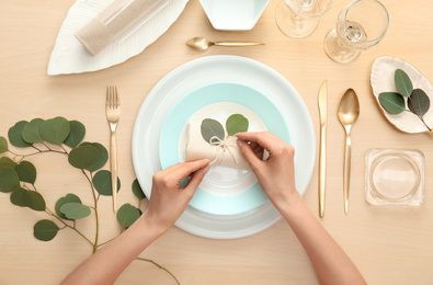 Woman setting table with green leaves for festive dinner, top view