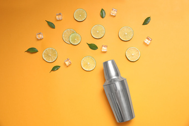 Flat lay composition with fresh juicy limes, ice cubes and cocktail shaker on yellow background