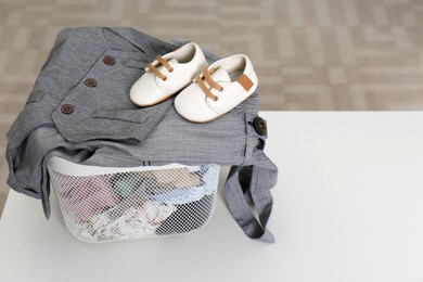 Photo of Laundry basket with baby clothes and shoes on white table indoors