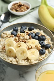 Tasty oatmeal with banana, blueberries, walnuts and milk served in bowl on white marble table, closeup