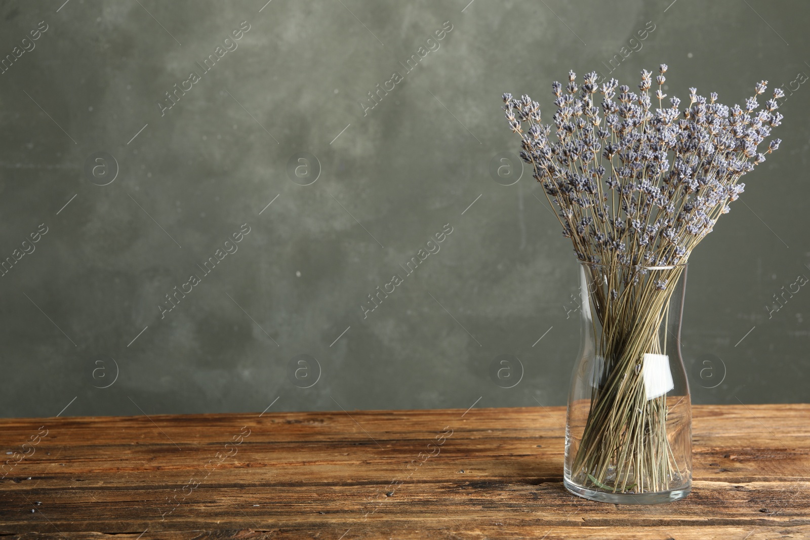 Photo of Dried lavender flowers in glass vase on wooden table against grey background. Space for text