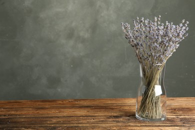 Photo of Dried lavender flowers in glass vase on wooden table against grey background. Space for text