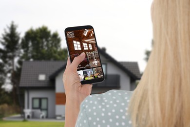 Woman using smart home security system on mobile phone near house outdoors. Device showing different rooms through cameras