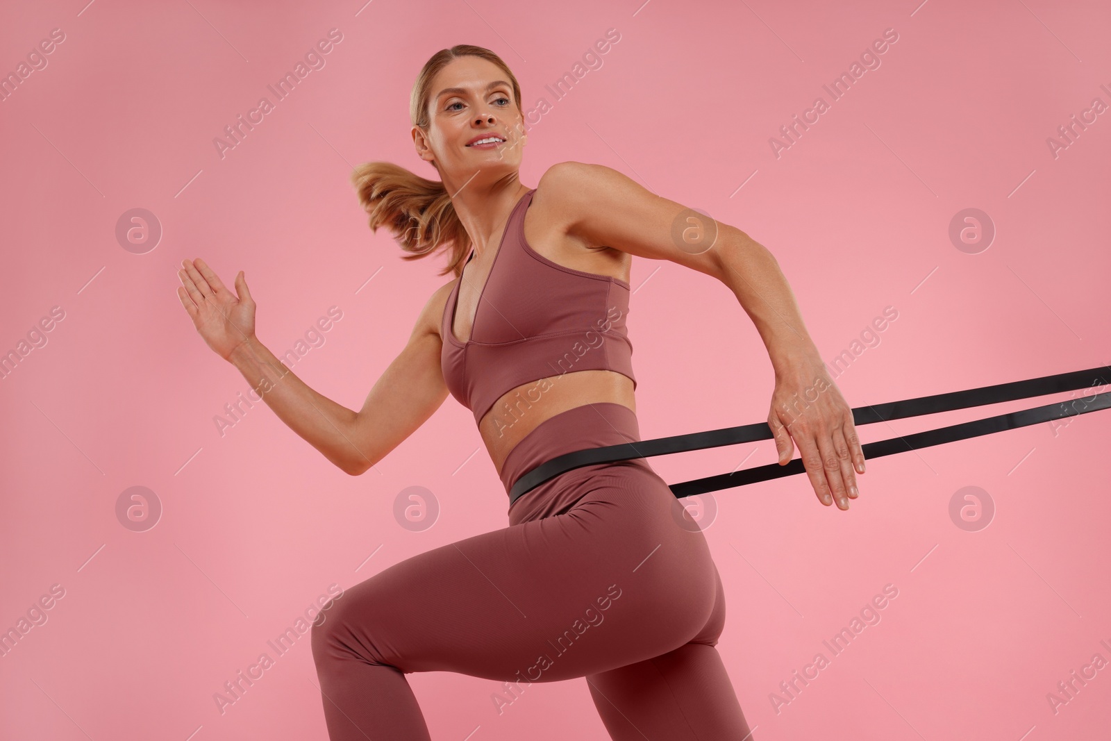 Photo of Woman exercising with elastic resistance band on pink background, low angle view