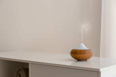 Photo of Aroma oil diffuser lamp on cabinet against light background