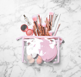 Cosmetic bag with makeup products and beauty accessories on white marble background, flat lay