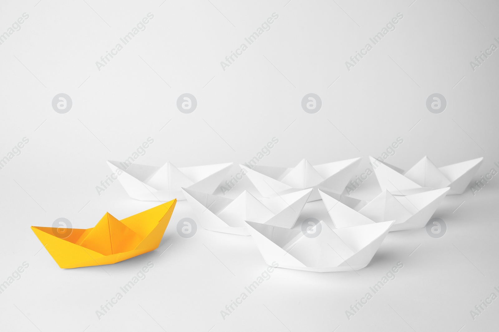 Photo of Group of paper boats following orange one on white background. Leadership concept