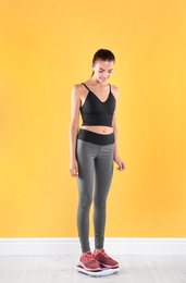 Photo of Happy young woman measuring her weight using scales near color wall. Weight loss motivation