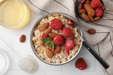 Delicious oatmeal with freeze dried strawberries, almonds and mint served on white tiled table, flat lay