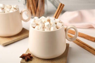 Photo of Cup of hot drink with marshmallows and aromatic cinnamon on white table