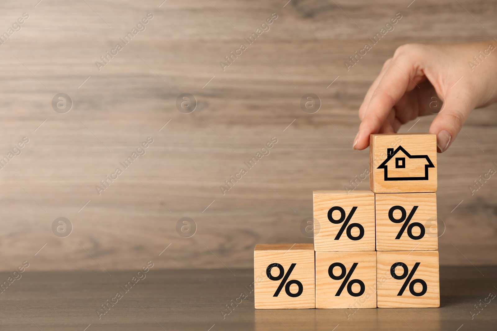 Image of Mortgage rate. Woman arranging cubes with house icon and percent signs at wooden table, closeup. Space for text