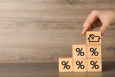 Image of Mortgage rate. Woman arranging cubes with house icon and percent signs at wooden table, closeup. Space for text