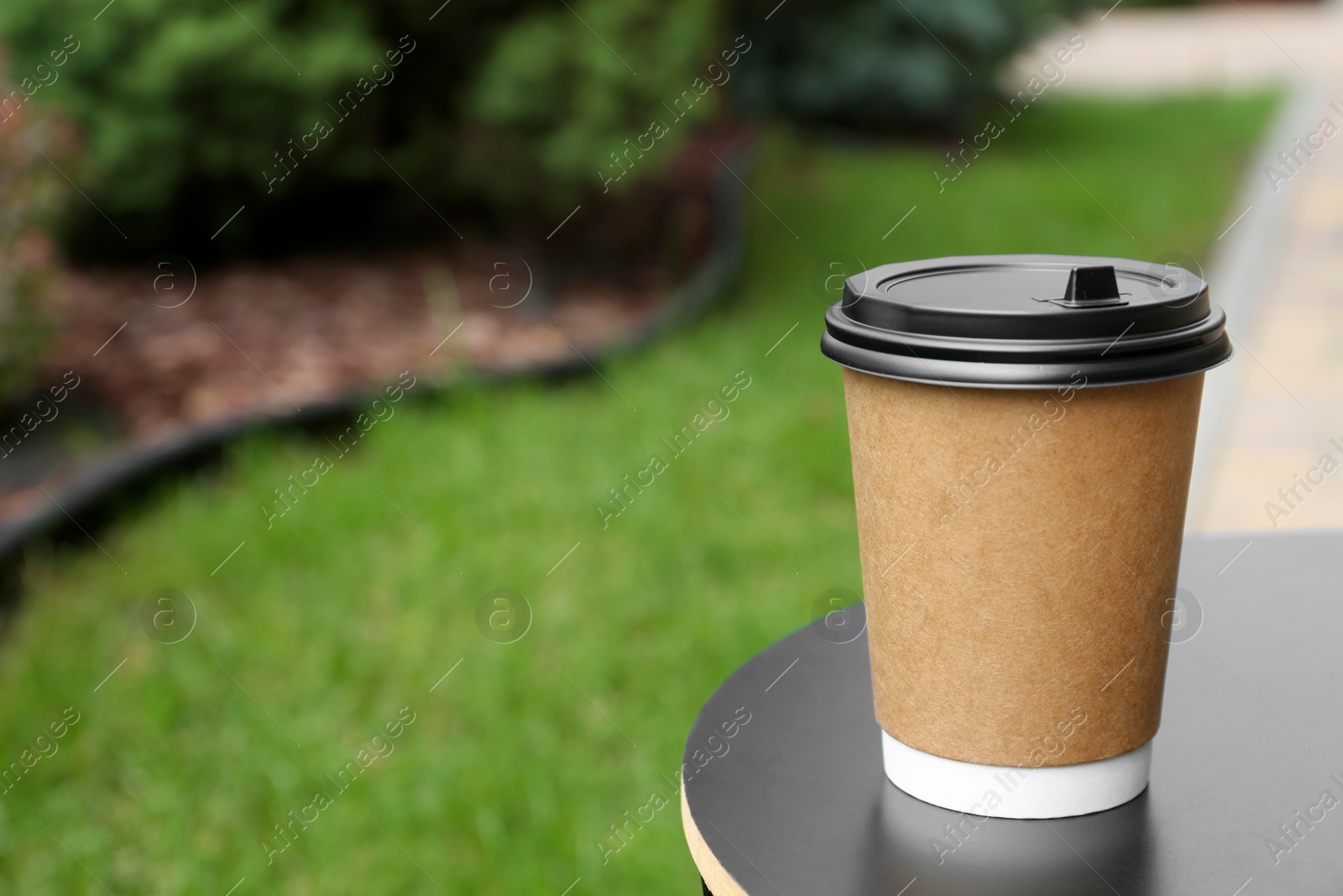 Photo of Cardboard cup with plastic lid on black table in park, space for text. Coffee to go