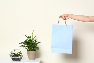 Woman with blank paper bag near white wall, closeup. Space for text