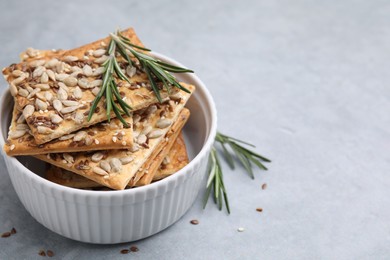 Photo of Cereal crackers with flax, sunflower, sesame seeds and rosemary in bowl on grey table, closeup. Space for text
