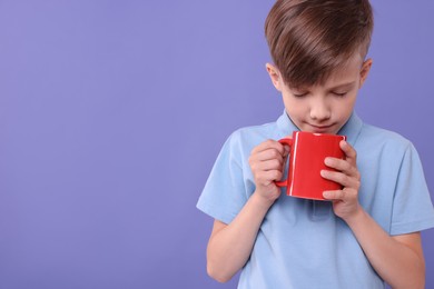 Photo of Cute boy with red ceramic mug on violet background, space for text