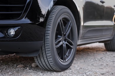 Modern black car parked on rubble road outdoors, closeup