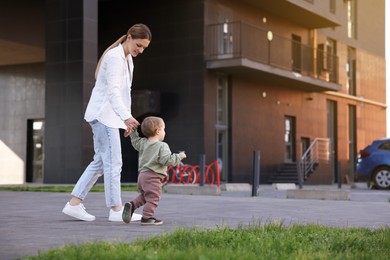 Happy nanny walking with cute little boy outdoors, space for text