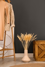 Photo of Dry plants near clothes rack indoors. Interior design