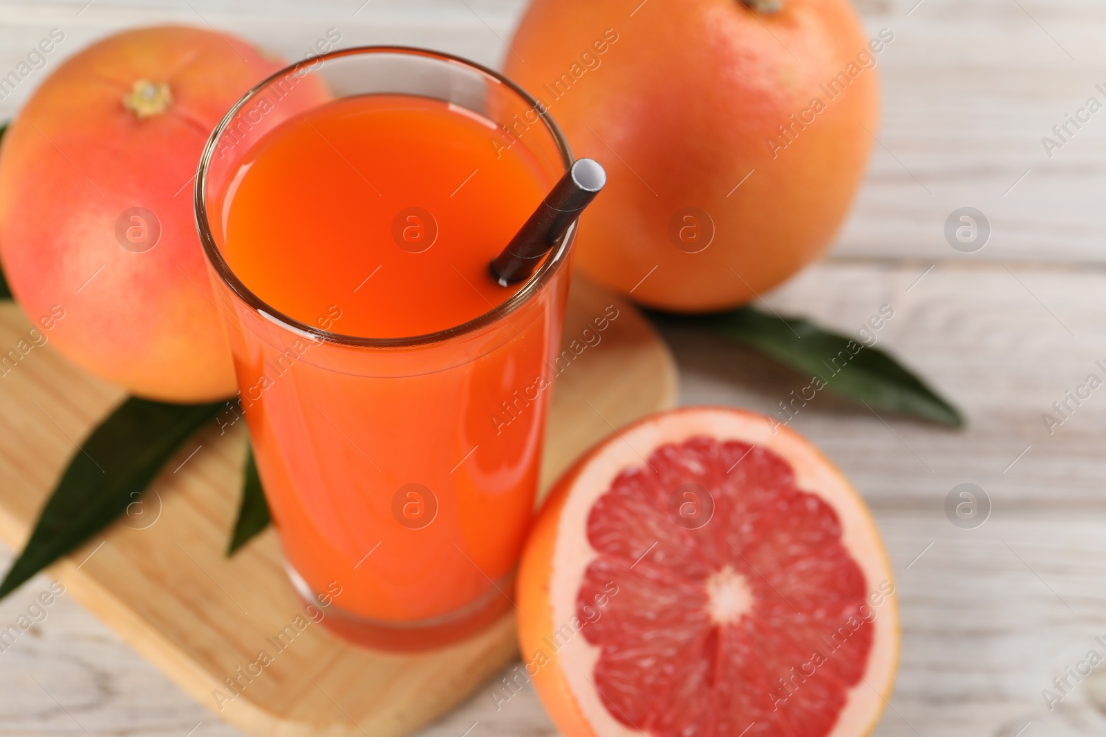 Photo of Tasty grapefruit juice in glass and fresh fruits on light wooden table, closeup. Space for text