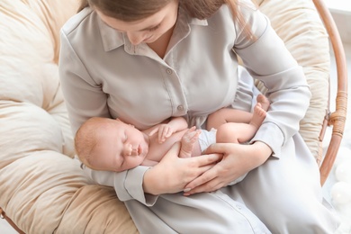 Young mother with her newborn baby in papasan chair at home