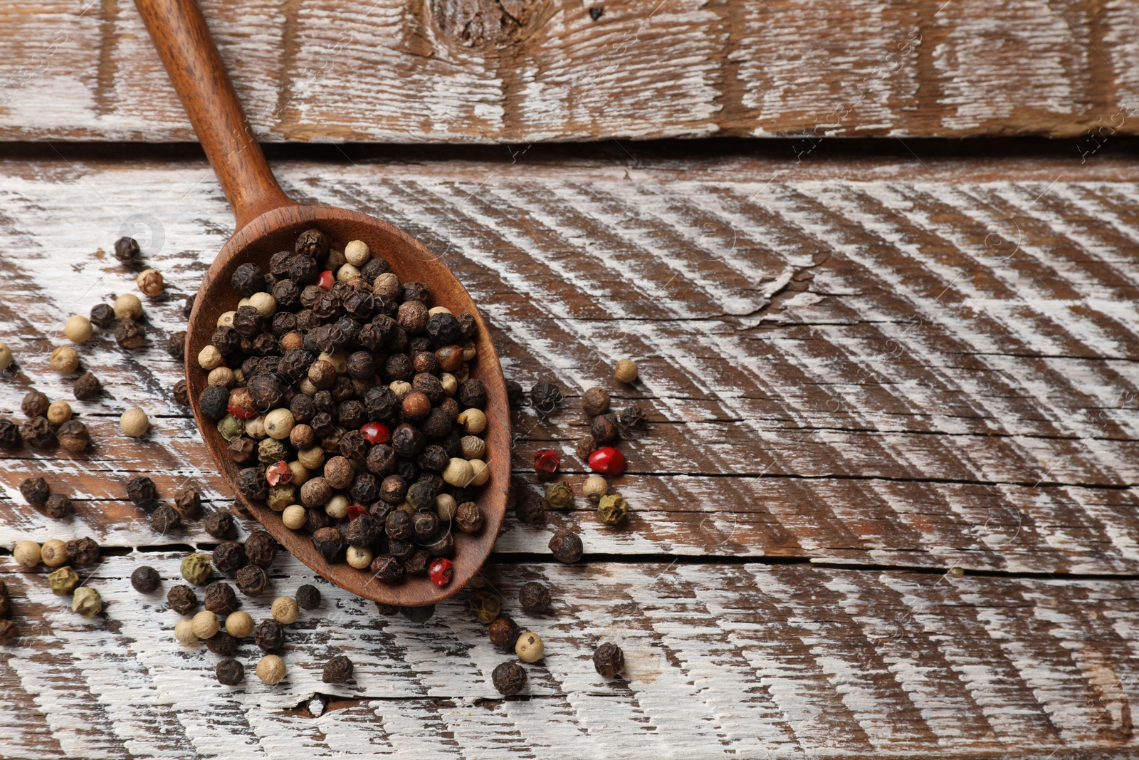 Photo of Aromatic spice. Different peppers in spoon on wooden table, top view. Space for text