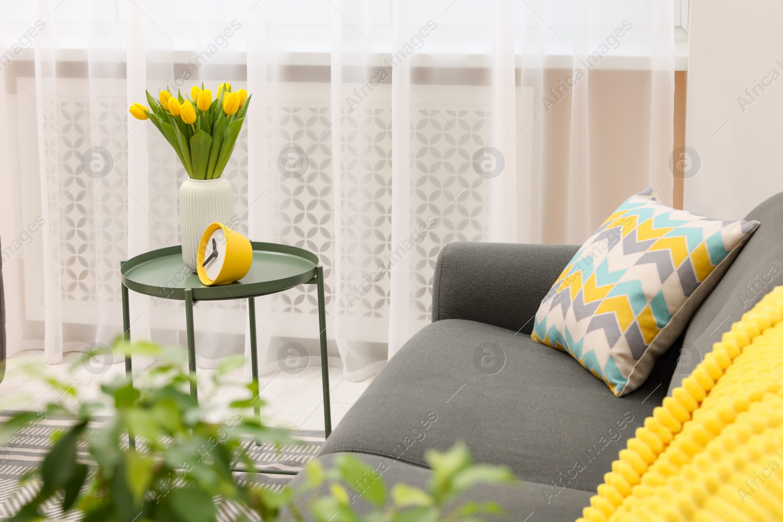 Photo of Spring atmosphere. Stylish living room interior with comfortable furniture and bouquet of beautiful yellow tulips