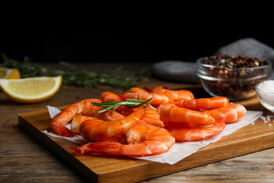 Photo of Delicious cooked shrimps with rosemary on wooden board