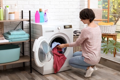 Photo of Young woman putting clothes into washing machine at home