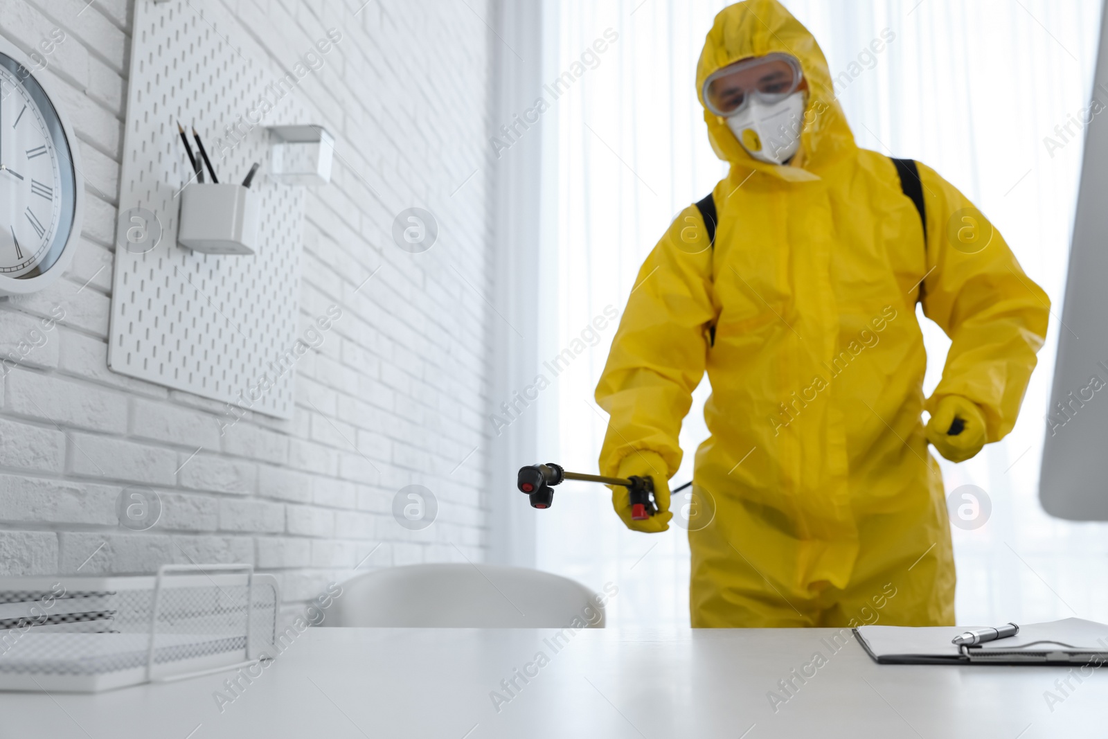 Photo of Employee in protective suit sanitizing office. Medical disinfection, focus on spray