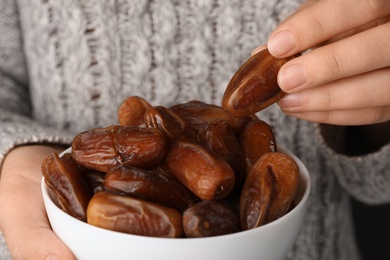 Photo of Woman holding bowl with tasty dried date fruits, closeup