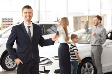 Salesman with key and young family in car salon