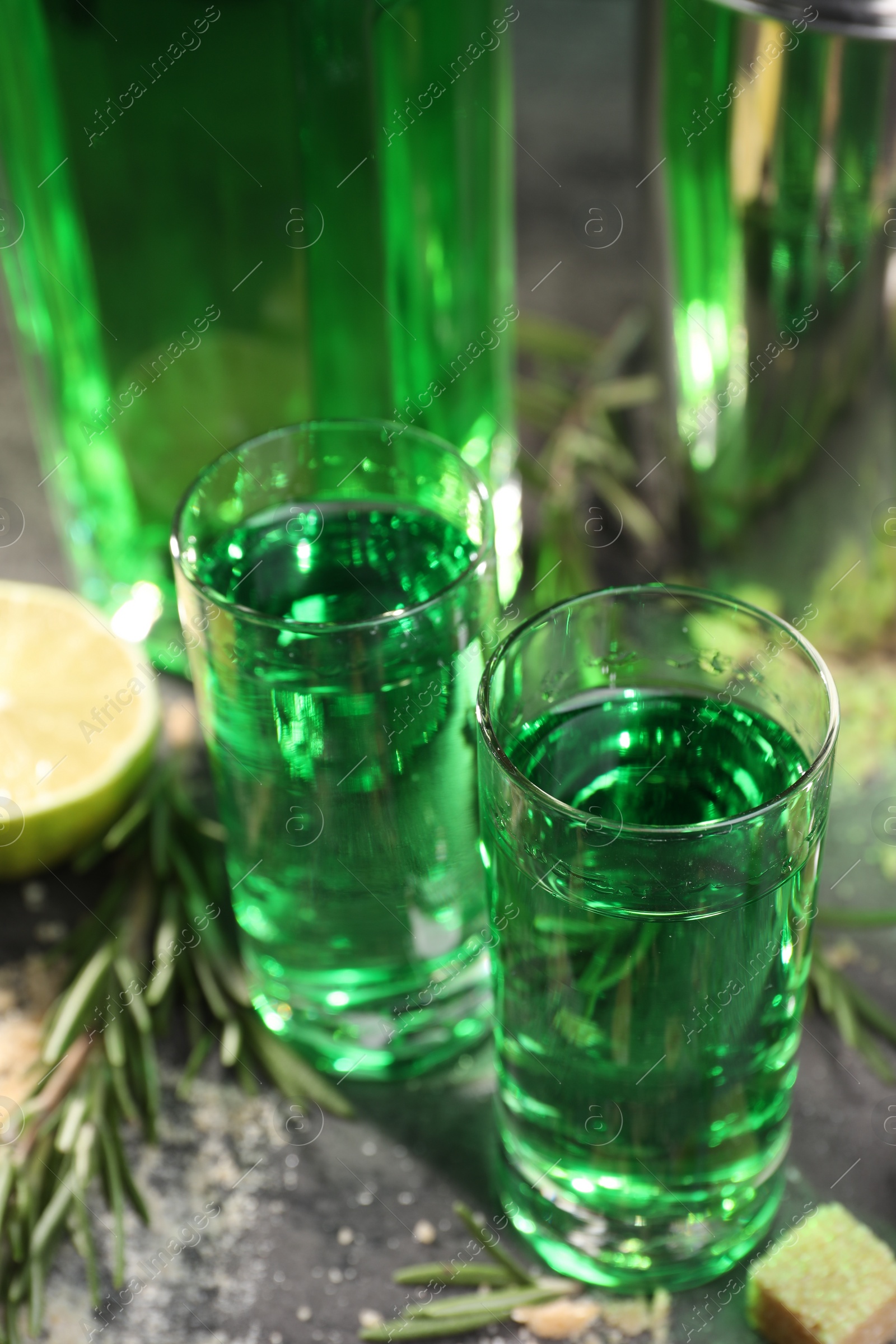 Photo of Absinthe in shot glasses on gray table, closeup. Alcoholic drink