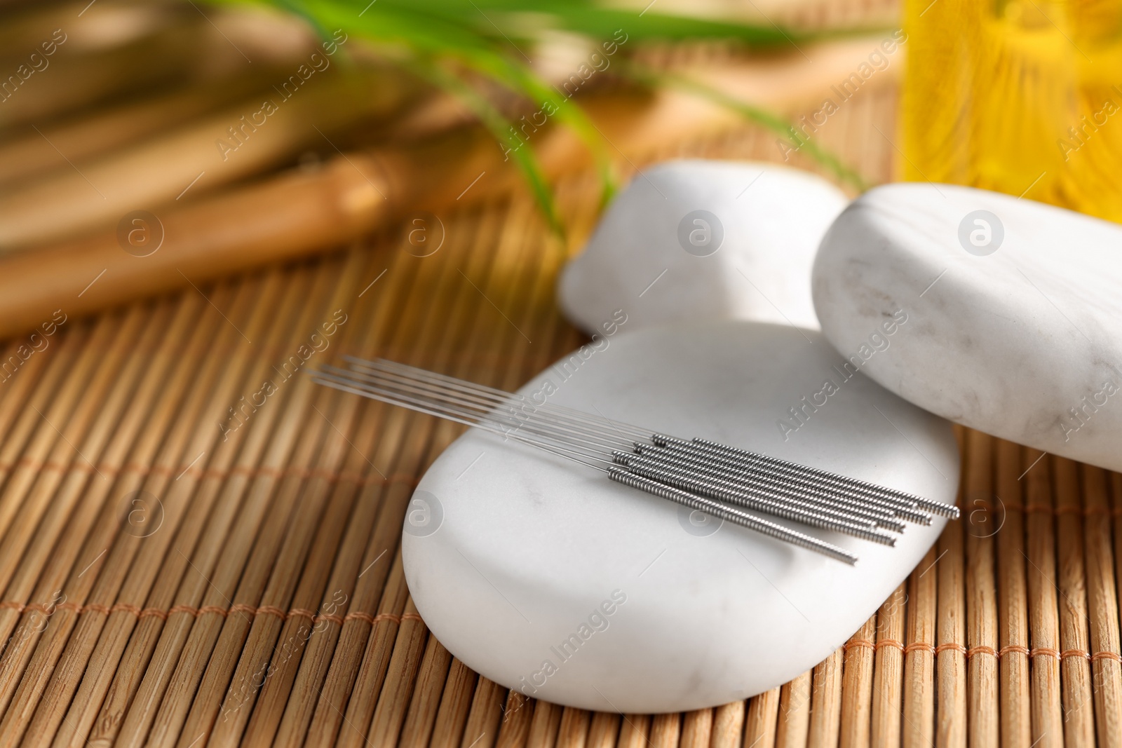 Photo of Acupuncture needles and spa stones on bamboo mat, closeup. Space for text