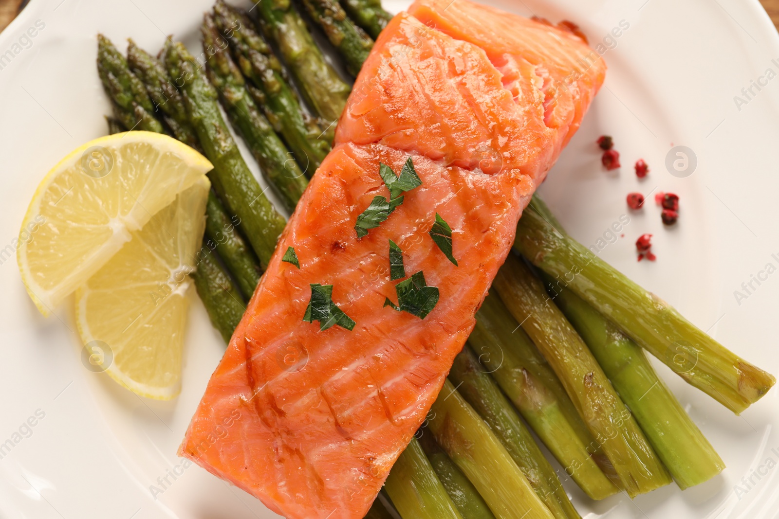 Photo of Plate with tasty grilled salmon, asparagus and lemon, top view