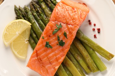 Photo of Plate with tasty grilled salmon, asparagus and lemon, top view