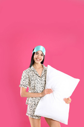 Young woman with pillow and sleep mask on pink background