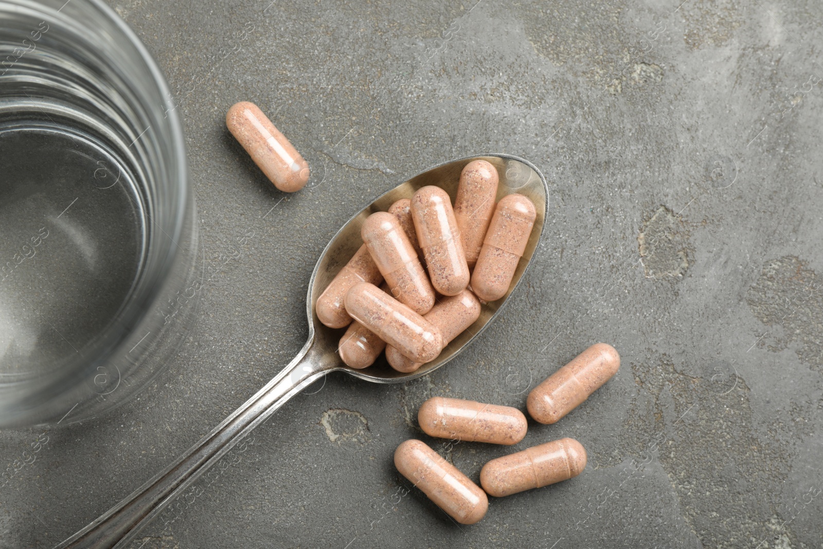 Photo of Gelatin capsules and glass of water on grey table, flat lay