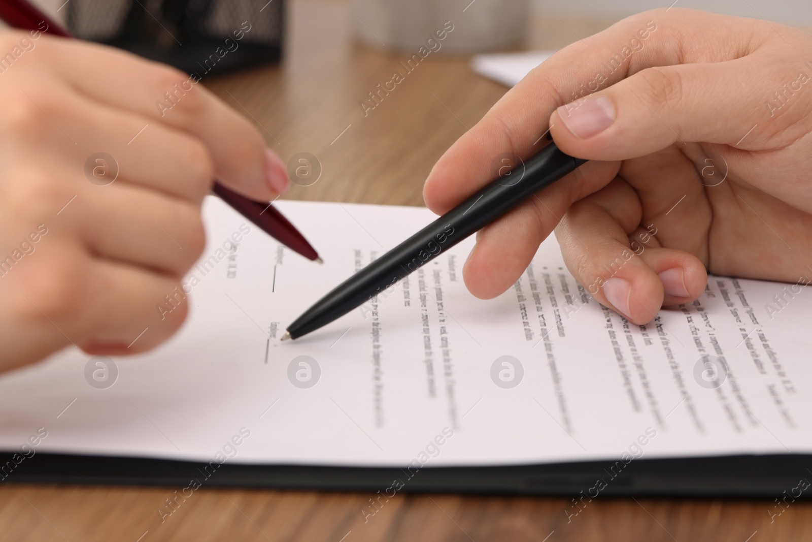 Photo of Man pointing at document and woman putting signature at wooden table, closeup