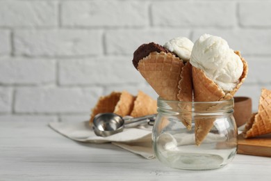Ice cream scoops in wafer cones on white wooden table against brick wall, space for text
