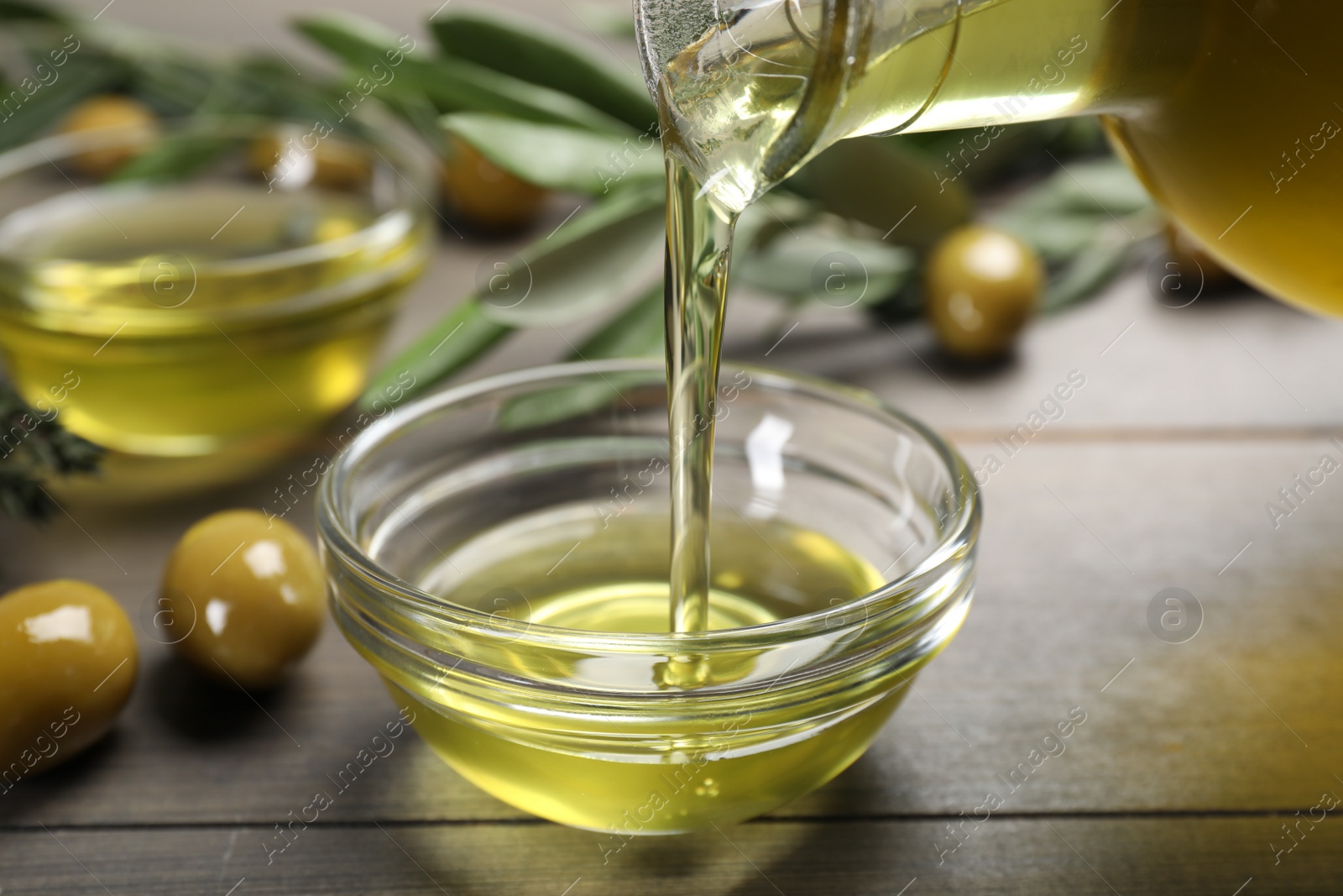 Photo of Pouring olive oil into bowl and olives on wooden table, closeup. Healthy cooking