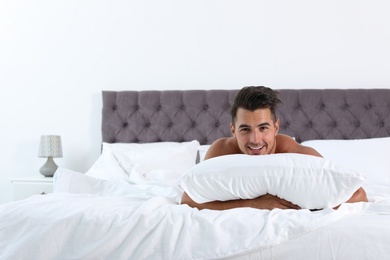 Photo of Sexy young man with soft pillow on bed at home