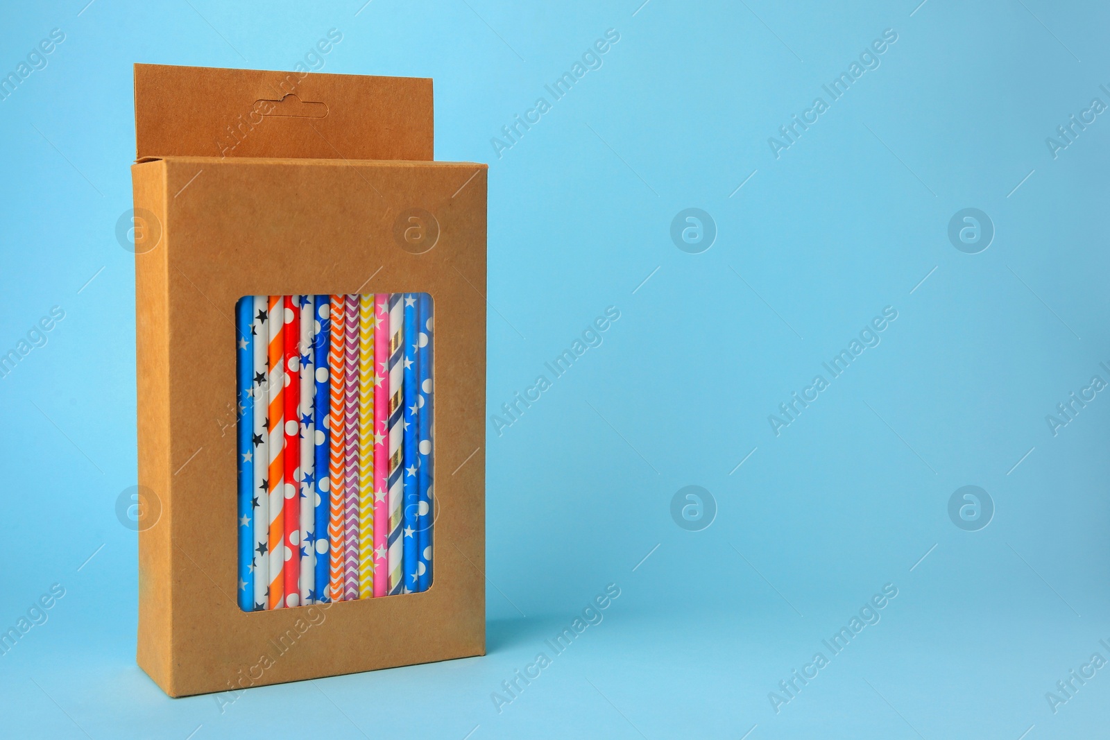 Photo of Box with many paper drinking straws on light blue background. Space for text